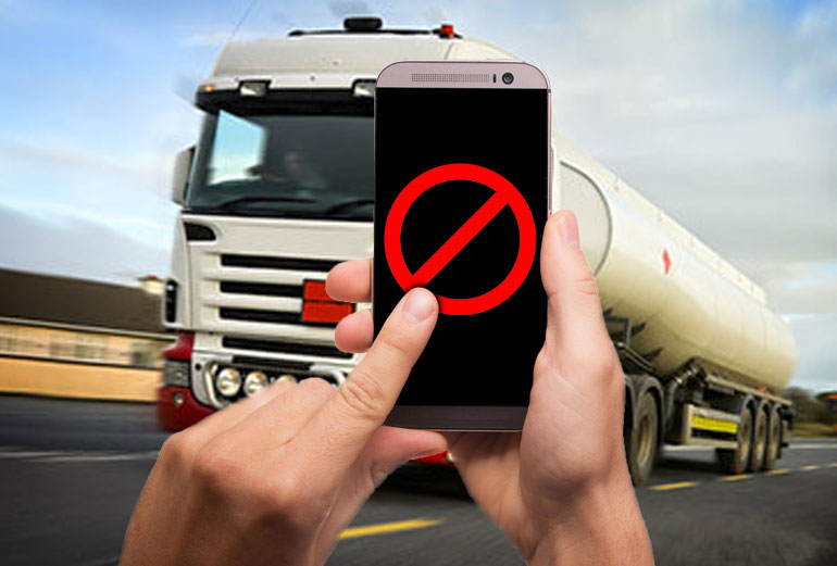 grafika przedstawia na pierwszym planie dłonie trzymające smartfon ze znakiem zakazu, a na drugim planie nadjeżdżającą ciężarówkę