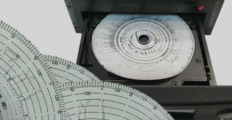 grafika przedstawia otwarty tachograf analogowy z papierowymi tarczkami